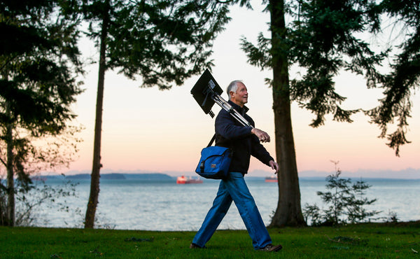 A person carrying a portable easel with a Maker's Bag slung cross-body.